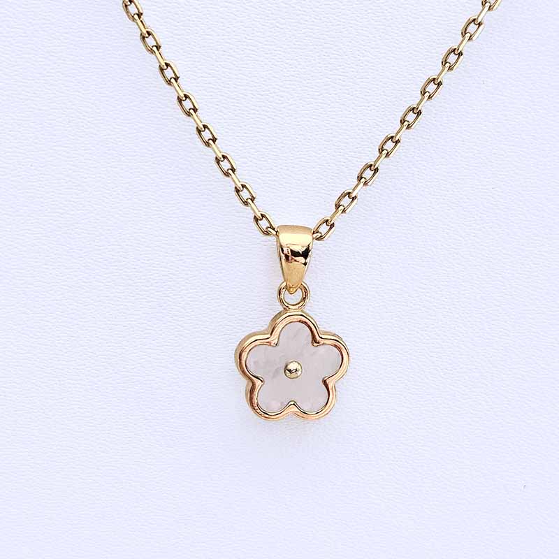 A gold-tone necklace with a five-petal flower pendant featuring a pale pink inlay and a small central gold bead, displayed on a textured white background.