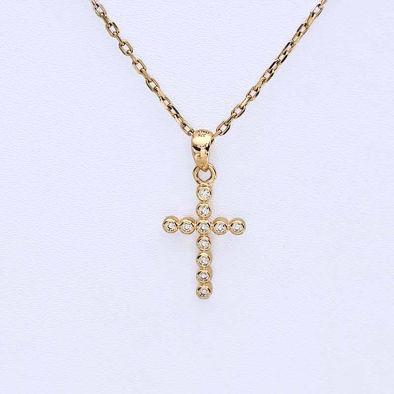 A gold cross pendant necklace adorned with small clear crystals, suspended from a gold chain on a light textured background.