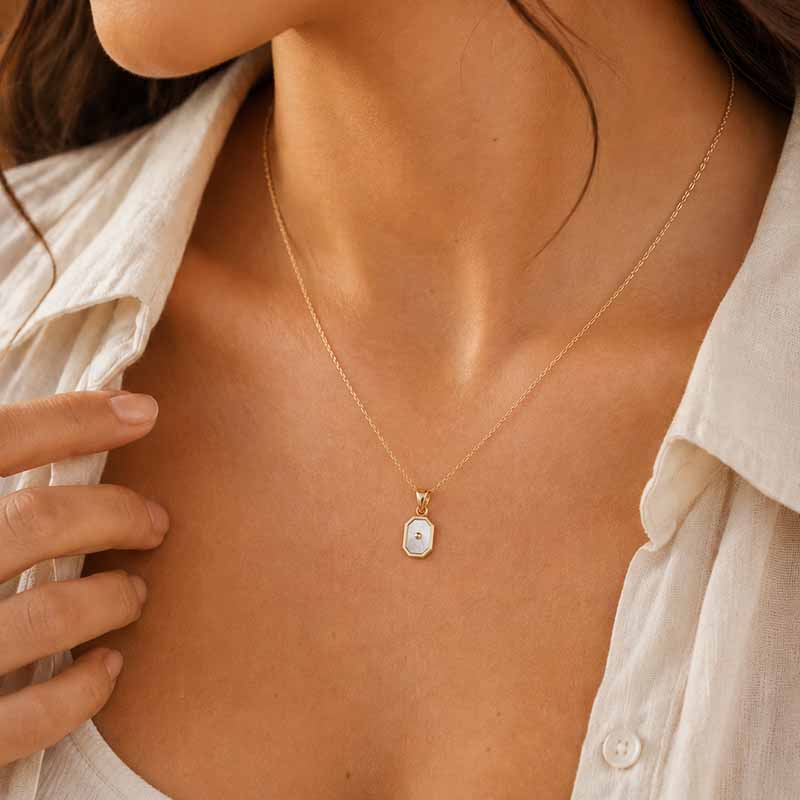 A close-up lifestyle shot of a model wearing a delicate gold chain necklace with a small mother of pearl pendant