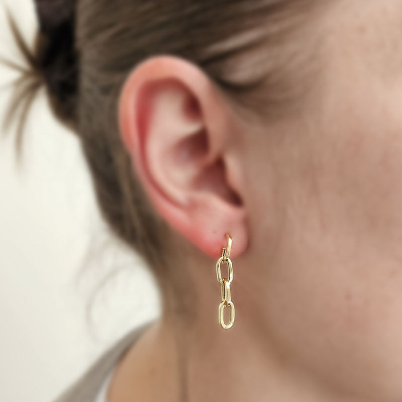 Close-up of a person wearing a gold chain earring with a blurred background