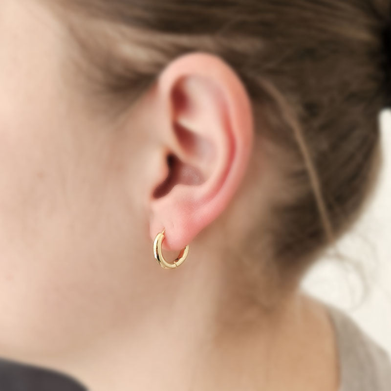 Close-up of a person wearing a gold hoop earring with a blurred background