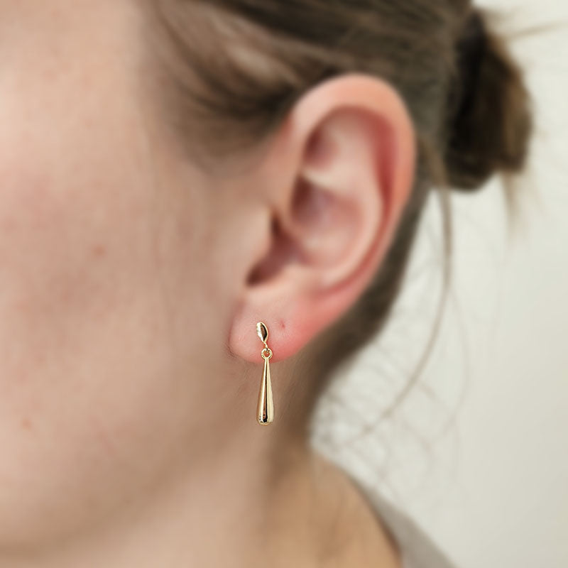 Gold teardrop earring worn by a person with a neutral background