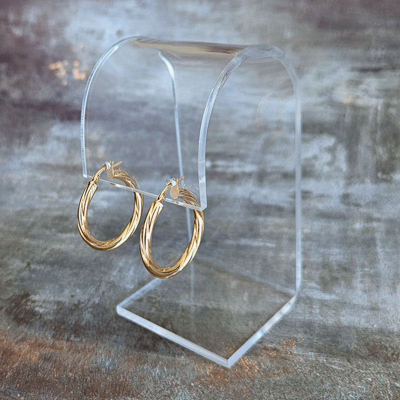 Gold hoop earrings on a clear stand against a textured gray background