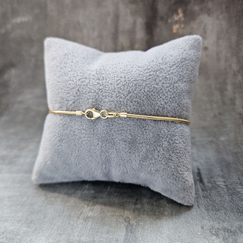 Gold bracelet on a gray textured pillow with a gray background