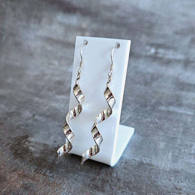 Silver spiral earrings on a white stand against a gray background