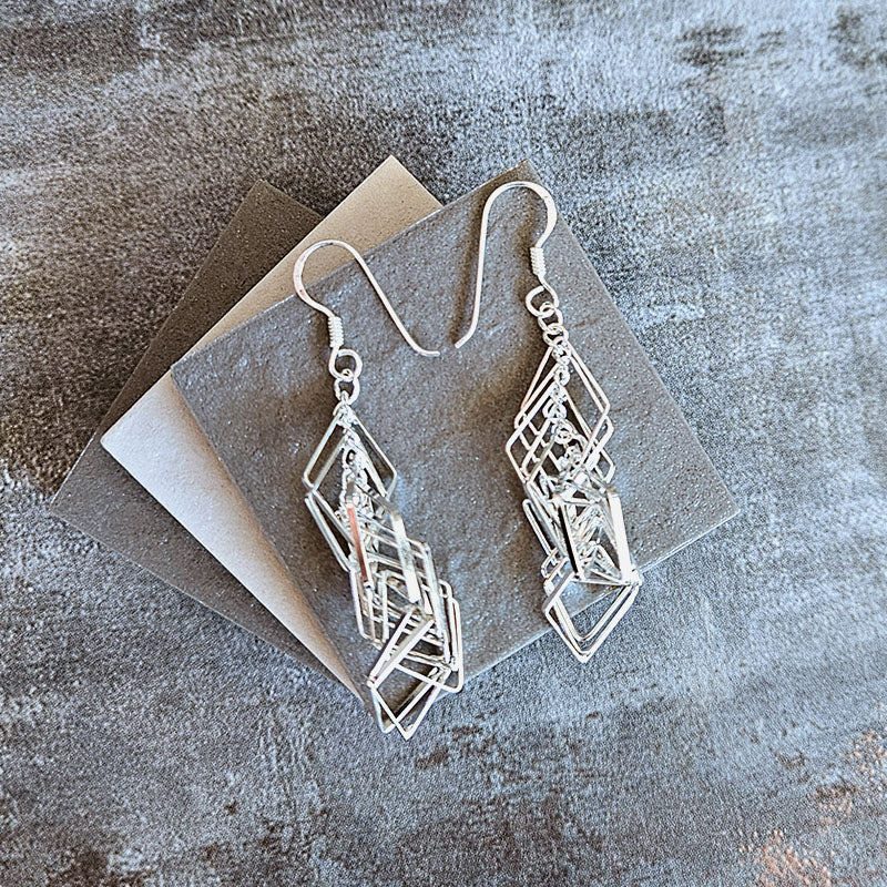 Silver geometric earrings on a textured surface