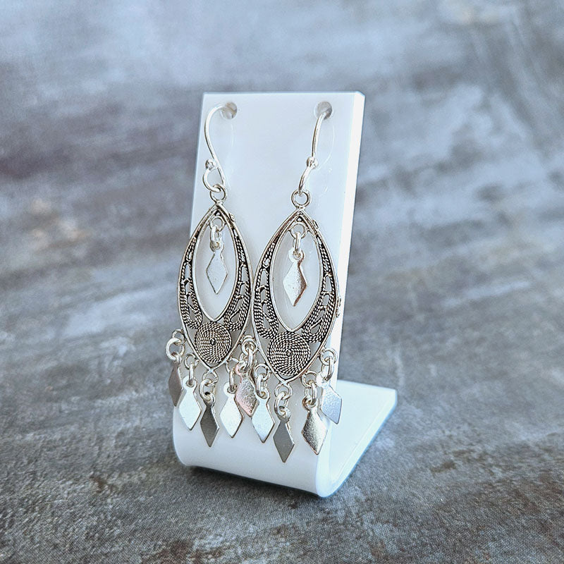Silver earrings on a white stand against a gray background