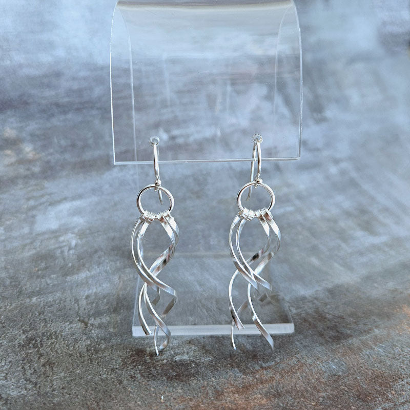 Silver earrings on a clear stand against a textured gray background
