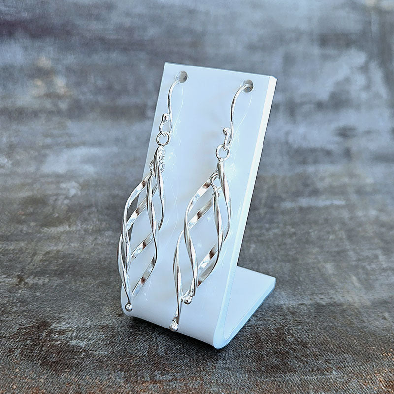 Silver earrings on a white stand against a textured gray background