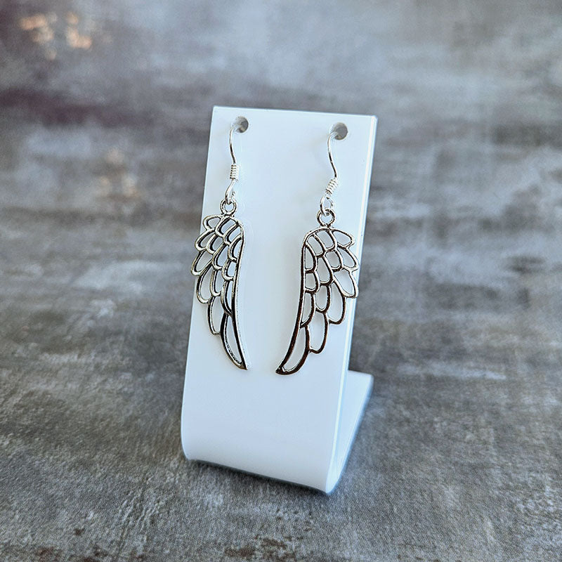 Wing-shaped earrings on a white card against a textured gray background