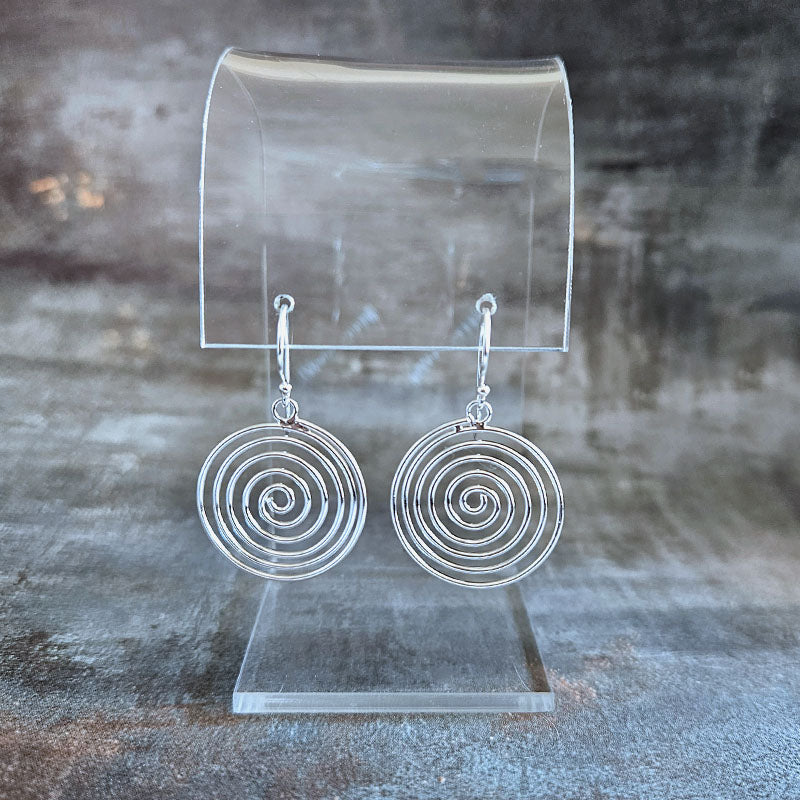 Silver spiral earrings on a clear stand against a textured gray background