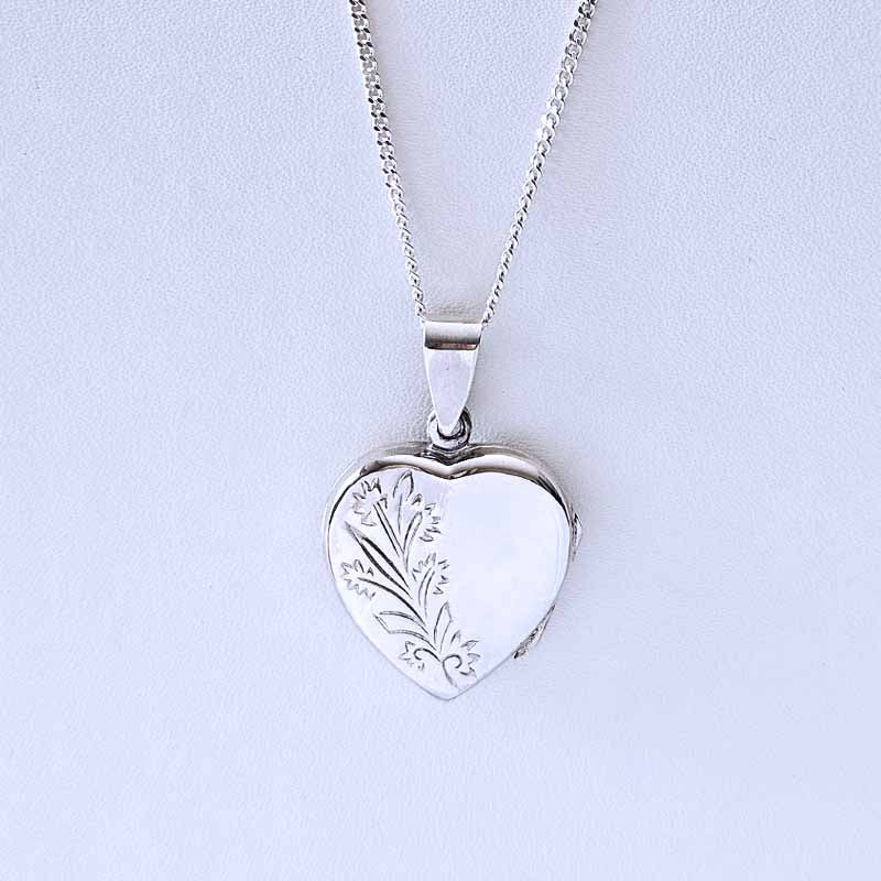 Silver heart-shaped locket with floral engraving on a light gray background