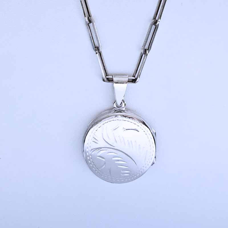 Silver locket with floral engraving on a light purple background