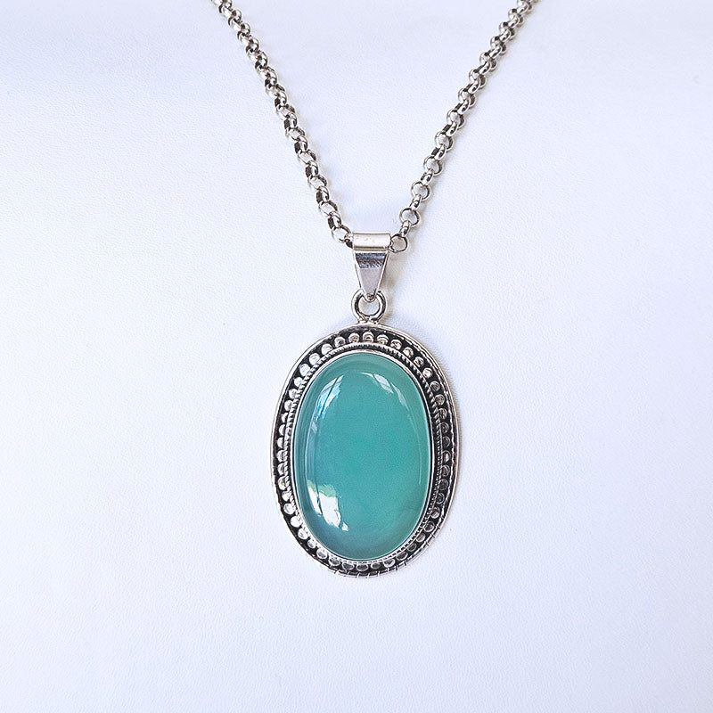An oval pendant necklace featuring a smooth, polished chalcedony stone in a silver-toned bezel setting, suspended from a matching silver chain against a plain white background.