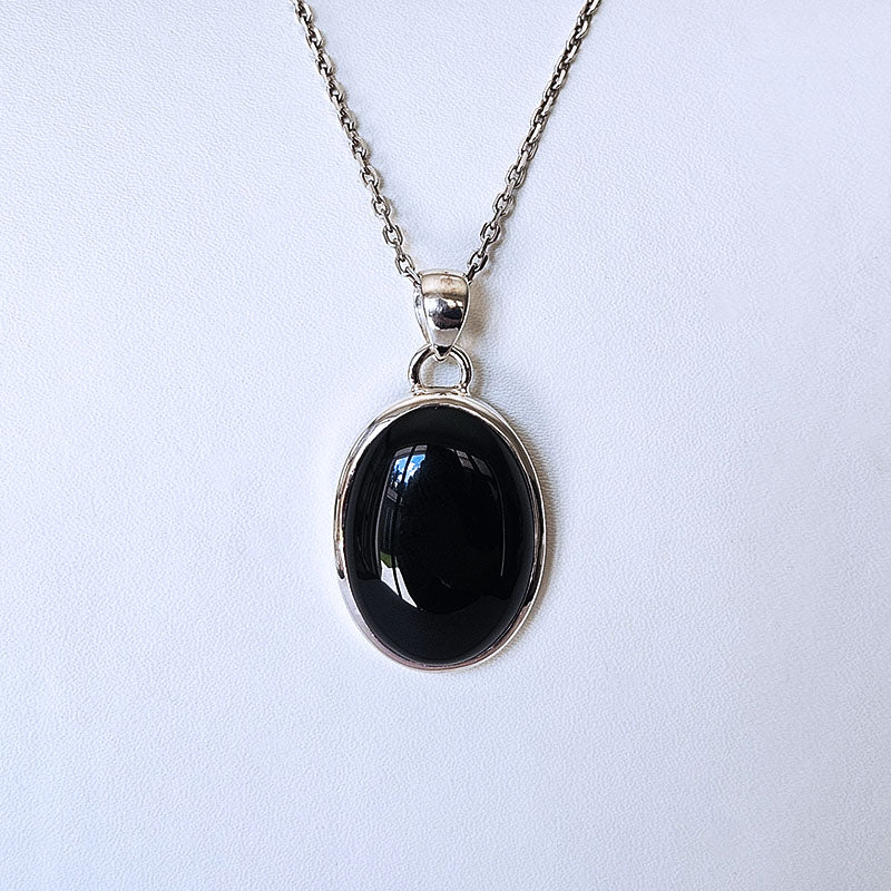 An oval black onyx pendant necklace in a silver bezel setting on a delicate silver chain, displayed against a light gray background.