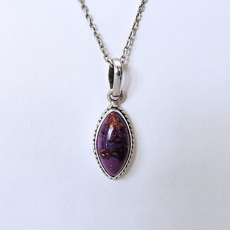 A silver chain necklace with an marquise bezel pendant containing a marbled turquoise stone with brown inclusions, set against a plain white background.
