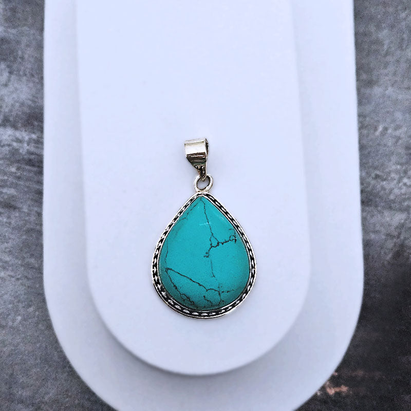 Teardrop-shaped Turquoise pendant set in sterling silver on a grey background