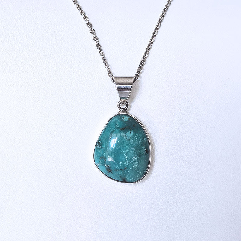 A silver necklace featuring a teardrop-shaped turquoise stone pendant, displayed against a clean white background.
