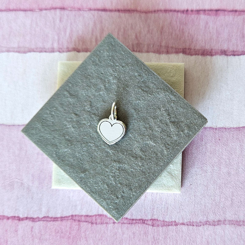 Silver heart-shaped charm on a gray card with a pink and white striped background
