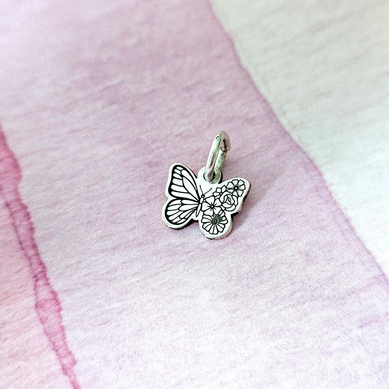 Silver butterfly charm on a pink fabric background