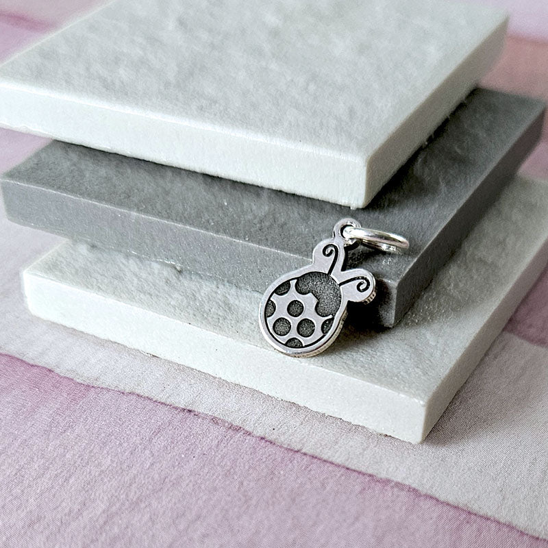 Silver ladybug charm with black pattern on a gray stone surface