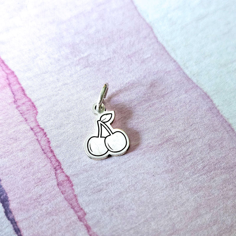 Silver cherry charm on a textured fabric background