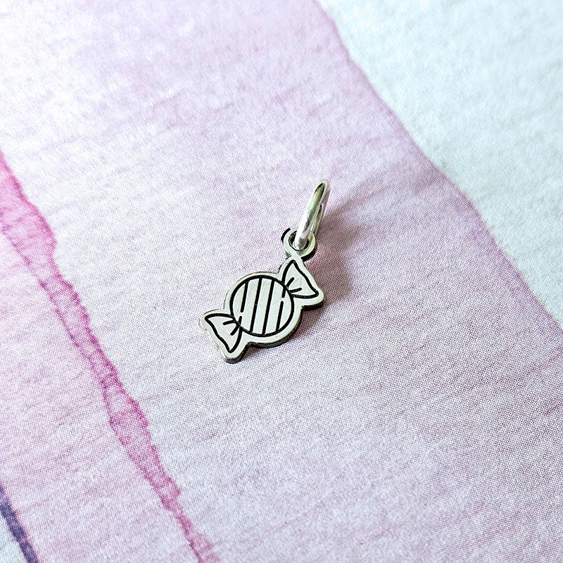 Silver candy-shaped charm on a pink fabric background