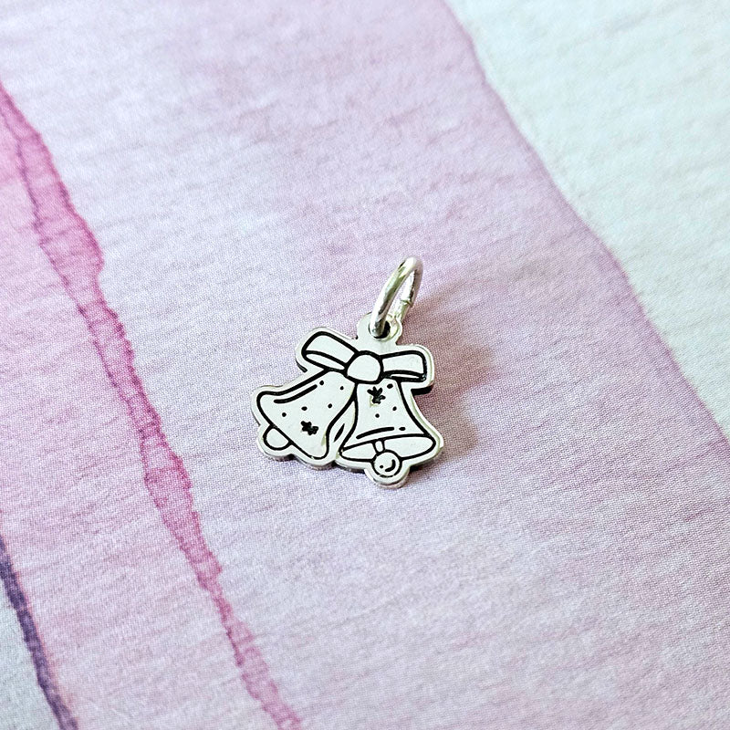 Silver bell charm with a bow on a pink fabric background