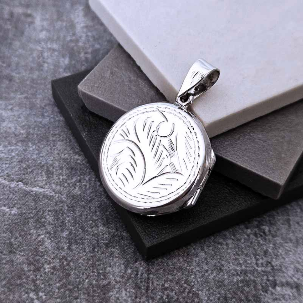 Sterling silver round locket with engraved feather design on grey stone background