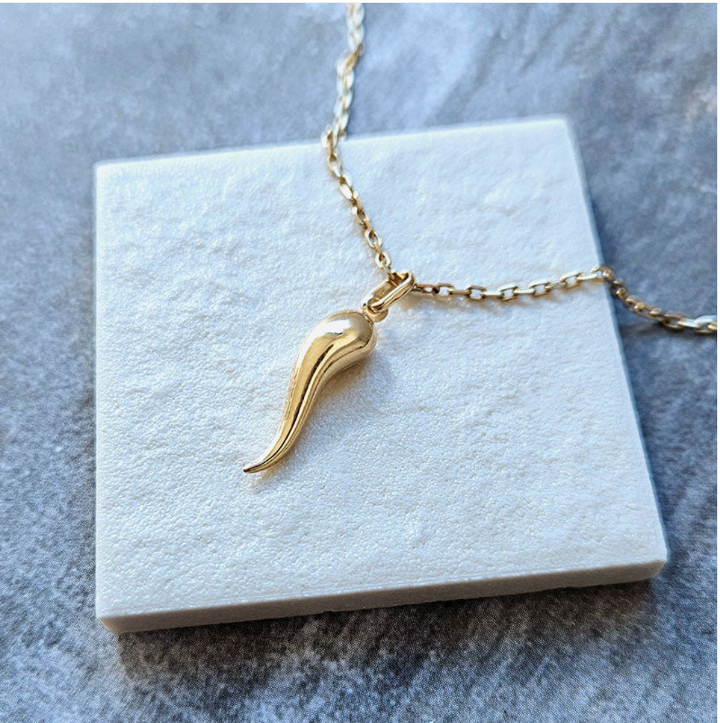 Gold cornicello pendant necklace on marble display