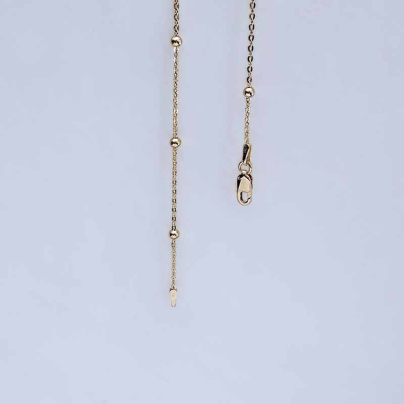 A close-up of a gold-toned chain necklace showing the extender chain with bead details and a lobster clasp on a light blue background.