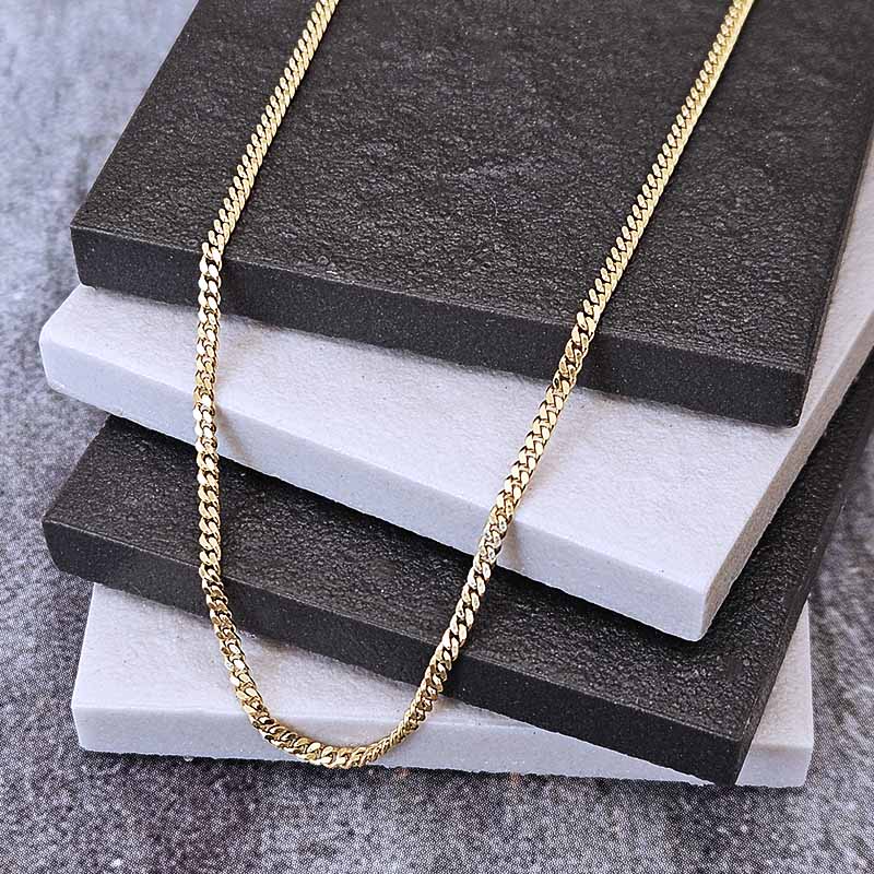 A gold-toned curb chain necklace draped over a stack of dark charcoal and white textured display blocks on a gray surface.