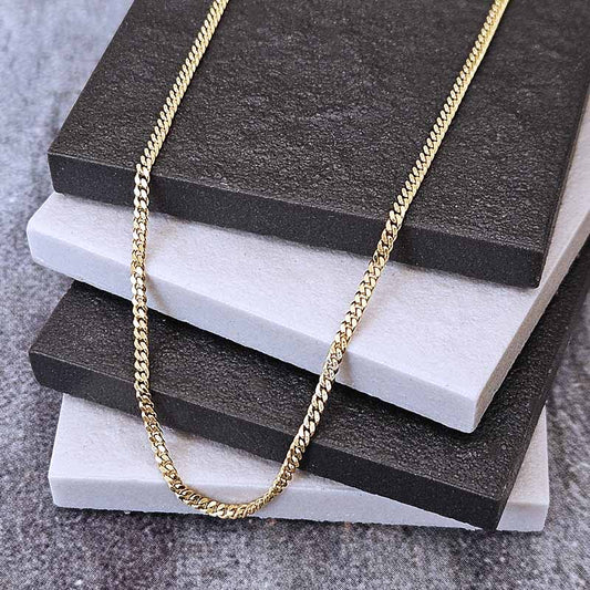 A gold-toned curb chain necklace draped over a stack of dark charcoal and white textured display blocks on a gray surface.