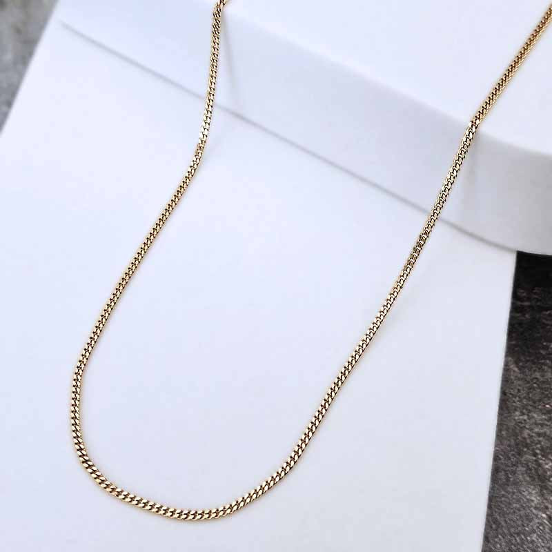 A gold-toned chain necklace draped over a white display stand, photographed close-up against a white background with a small dark textured area at the lower right.