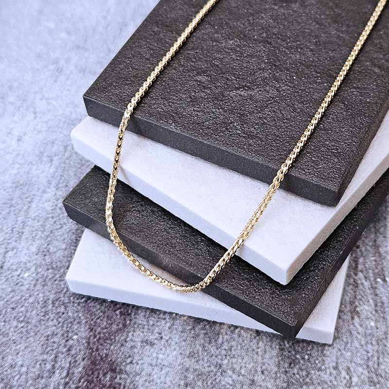 A delicate gold chain necklace draped over a stack of textured square tiles, with the chain clearly visible against a gray stone-like surface.