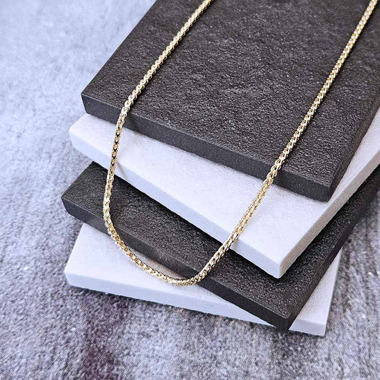 A delicate gold chain necklace draped over a stack of textured square tiles, with the chain clearly visible against a gray stone-like surface.