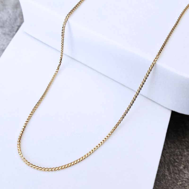 A gold-colored twisted rope chain necklace draped over a white display block.