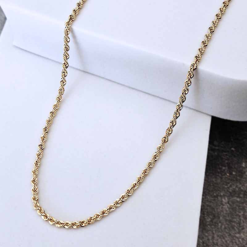 A gold twisted rope chain necklace draped over a white display block.