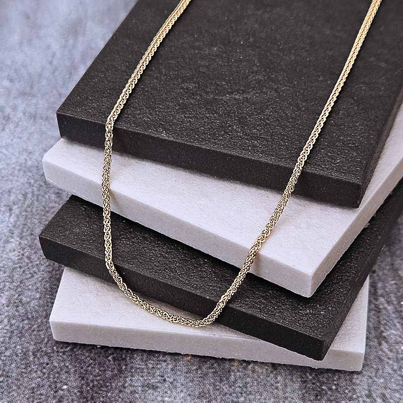 A gold chain necklace draped over stacked black and white display blocks on a gray textured surface.