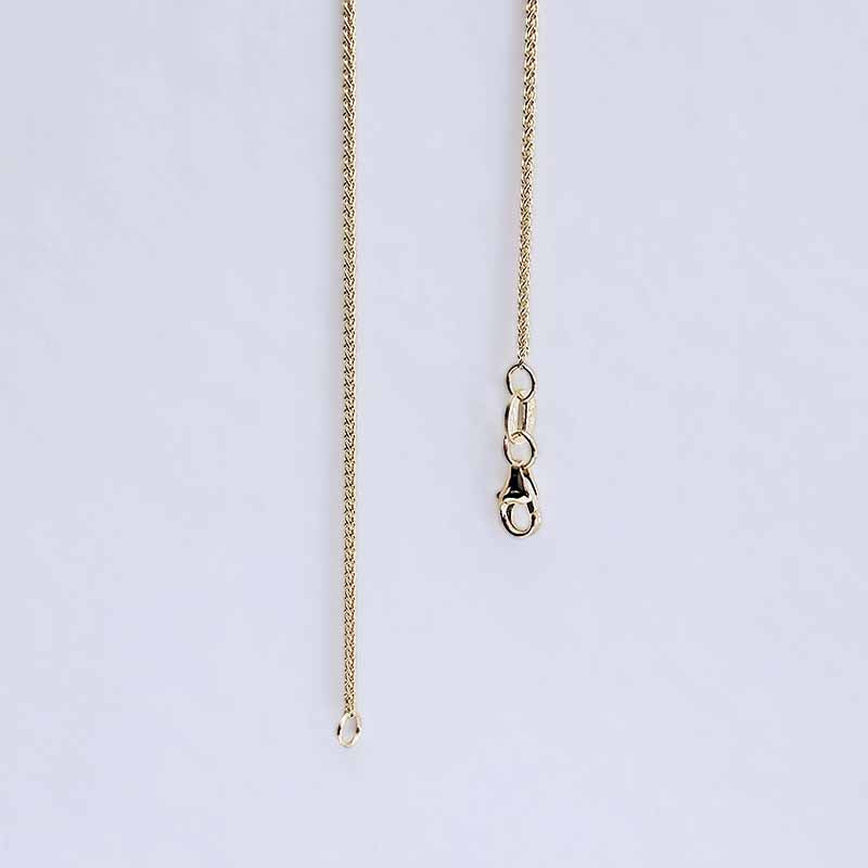 A close-up of a gold chain necklace showing the extender section with a lobster clasp on a light gray background.