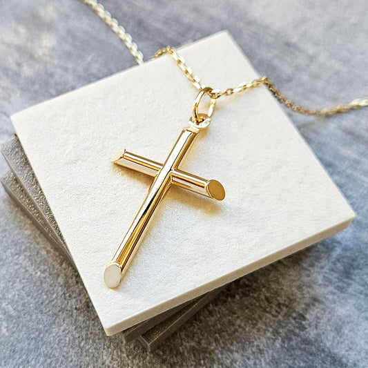 Gold cross necklace on a white card with a gray background