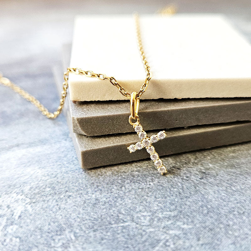 Gold necklace with a cross pendant on a gray surface