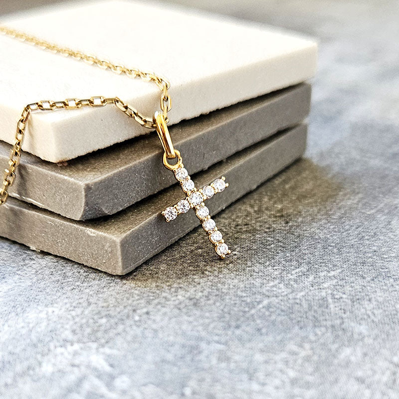 Gold necklace with a diamond cross pendant on a textured surface