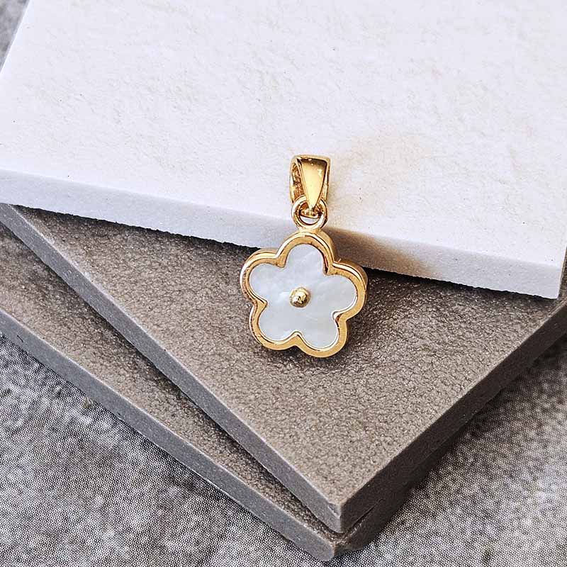 A gold flower-shaped pendant with a white mother-of-pearl center, displayed on stacked gray and white textured blocks.