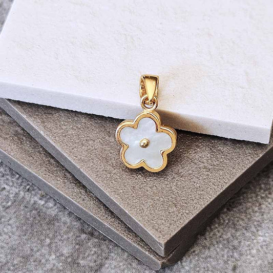 A gold flower-shaped pendant with a white mother-of-pearl center, displayed on stacked gray and white textured blocks.