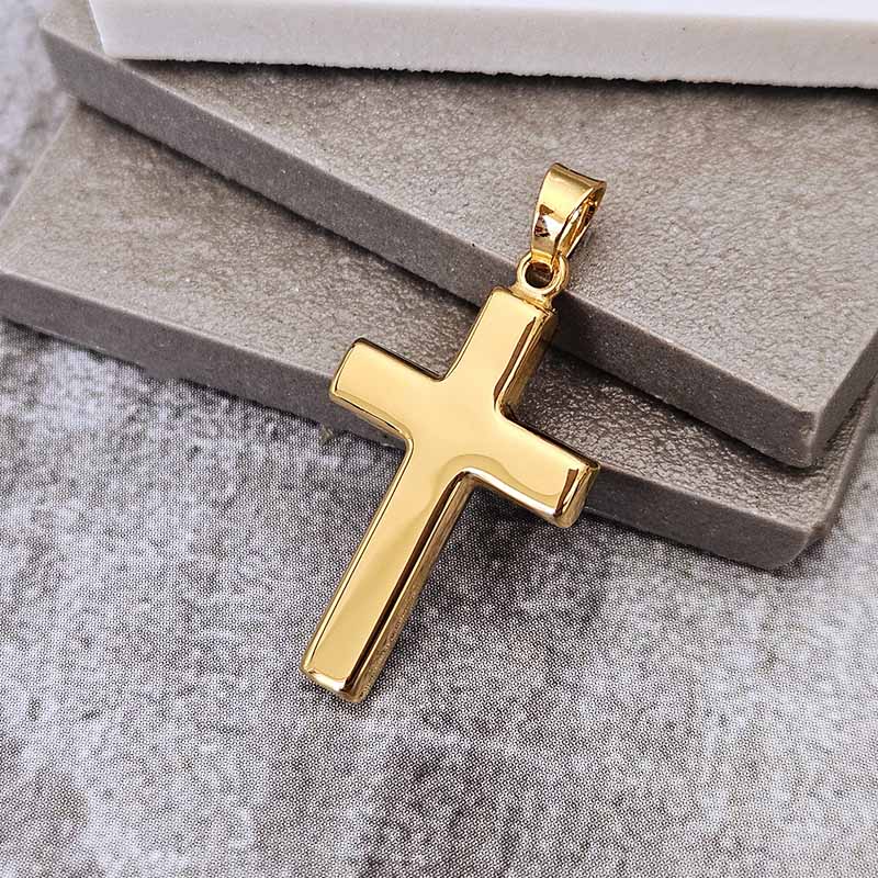 A polished gold cross pendant with a smooth, rectangular design and a matching bail, resting on a textured gray display cushion.