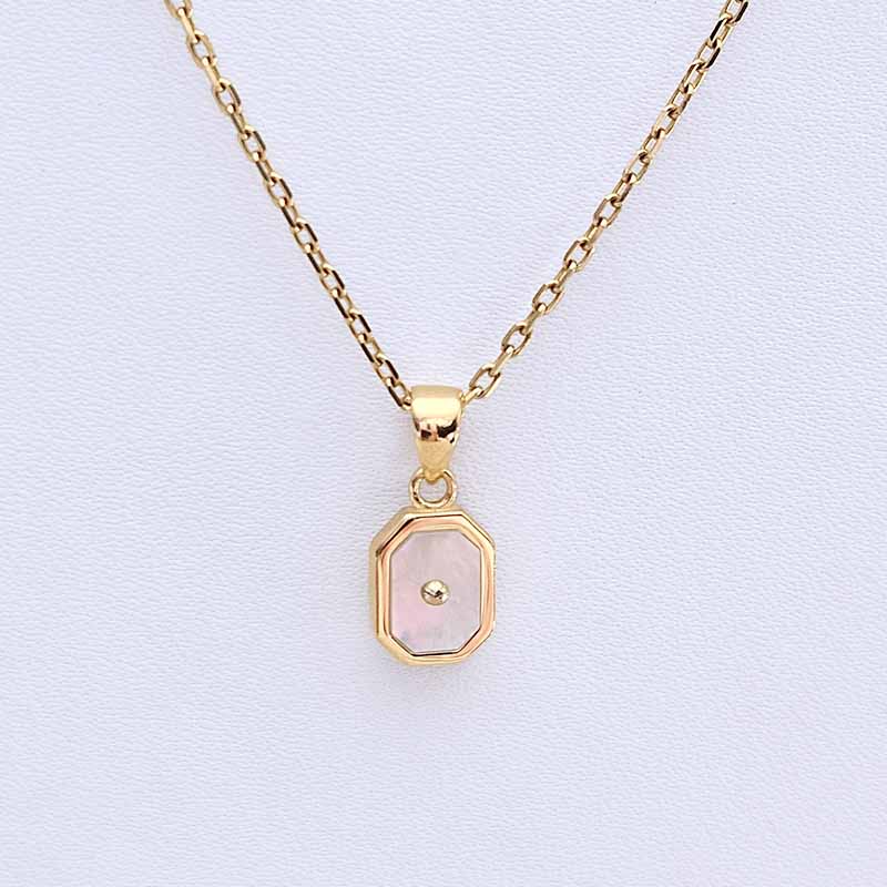 A gold chain necklace with an octagonal pendant featuring a pale pink inlay and a small central gold dot, displayed on a light textured background.