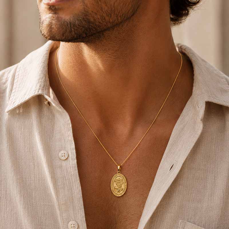 A close-up of a man wearing a gold oval pendant necklace with an embossed religious figure, styled with a light beige linen shirt.