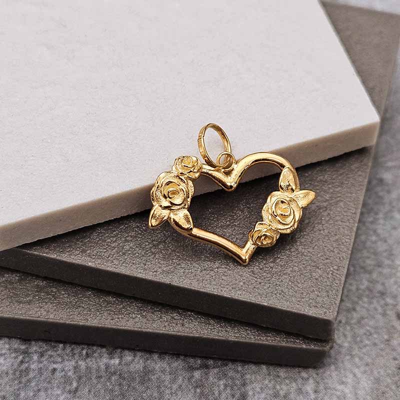 A gold heart-shaped pendant with rose details, displayed on a stack of gray and white textured stone tiles.