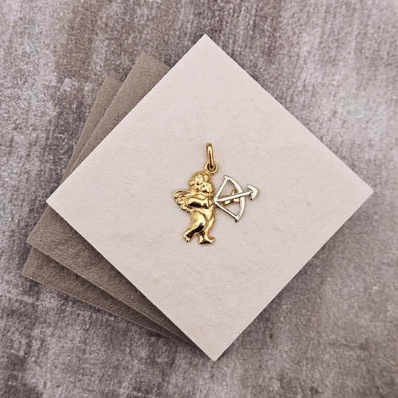 A small gold cupid charm holding a bow and arrow, displayed on a stacked set of textured square cards over a gray stone-like surface.